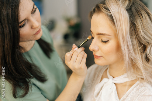 Professional makeup artistes working with beautiful young woman in dressing room, in front of mirror. Concept of backstage work.