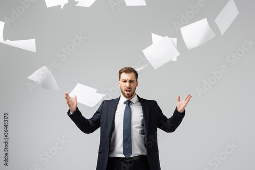 Obraz na płótnie displeased businessman in suit throwing papers in air isolated on grey