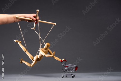 Cuadro en lienzo cropped view of puppeteer holding wooden marionette with shopping cart on black