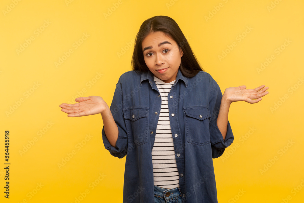 Have no idea, maybe! Portrait of confused girl in denim shirt shrugging shoulders in bewilderment, doubting and feeling uncertain, don't know answer. indoor studio shot isolated on yellow background Have no idea, maybe! Portrait of confused girl in denim shirt shrugging shoulders in bewilderment, doubting and feeling uncertain, don't know answer. indoor studio shot isolated on yellow background