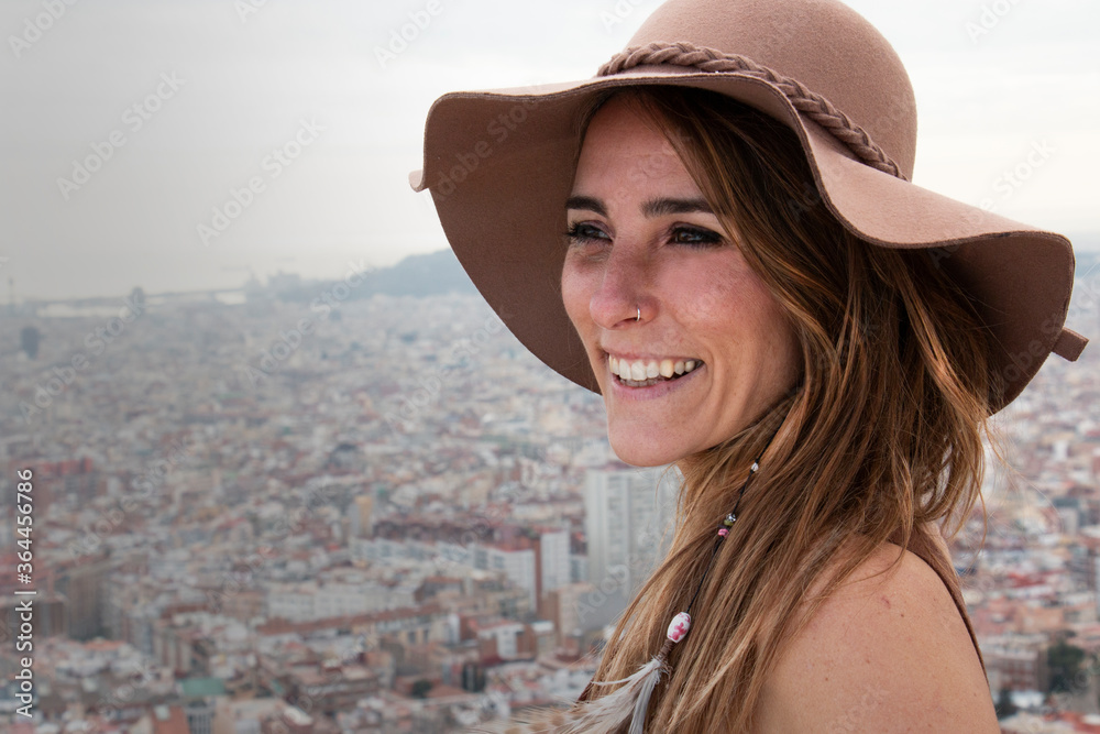 smiling girl with hat in a viewpoint from which the city of Barcelona is seen in the background