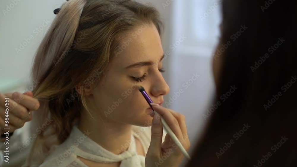Close-up of face of young pretty woman getting professional make-up service from makeup artist and hairdresser in beauty salon. Concept of beauty, fashion and stylish makeup. Shooting in slow motion. Close-up of face of young pretty woman getting professional make-up service from makeup artist and hairdresser in beauty salon. Concept of beauty, fashion and stylish makeup. Shooting in slow motion.