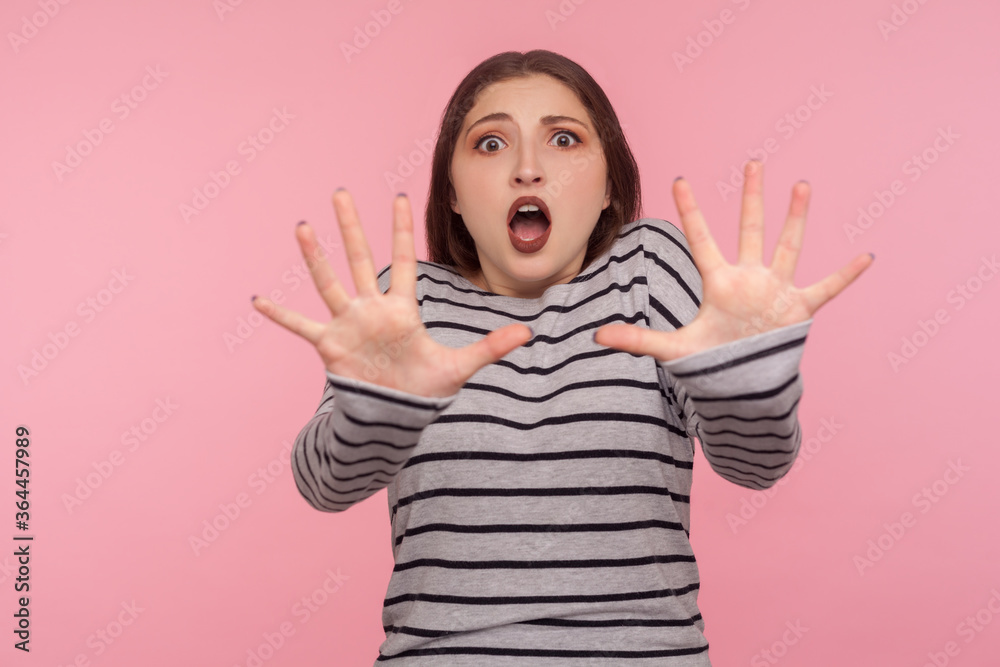 Panic and phobia. Portrait of scared woman in striped sweatshirt raising hands from sudden fear, looking terrified, scared to death, horror facial expression. studio shot isolated on pink background Panic and phobia. Portrait of scared woman in striped sweatshirt raising hands from sudden fear, looking terrified, scared to death, horror facial expression. studio shot isolated on pink background