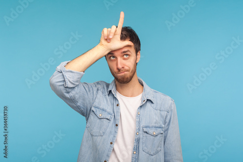 Obraz na plátně I lost job! Portrait of depressed man in worker denim shirt showing loser gesture, L finger sign on forehead, upset about dismissal, unlucky day