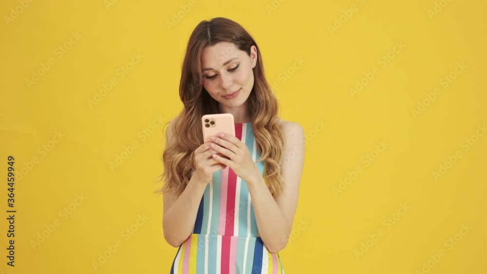 A focused nice woman is using her smartphone standing isolated over a yellow background A focused nice woman is using her smartphone standing isolated over a yellow background