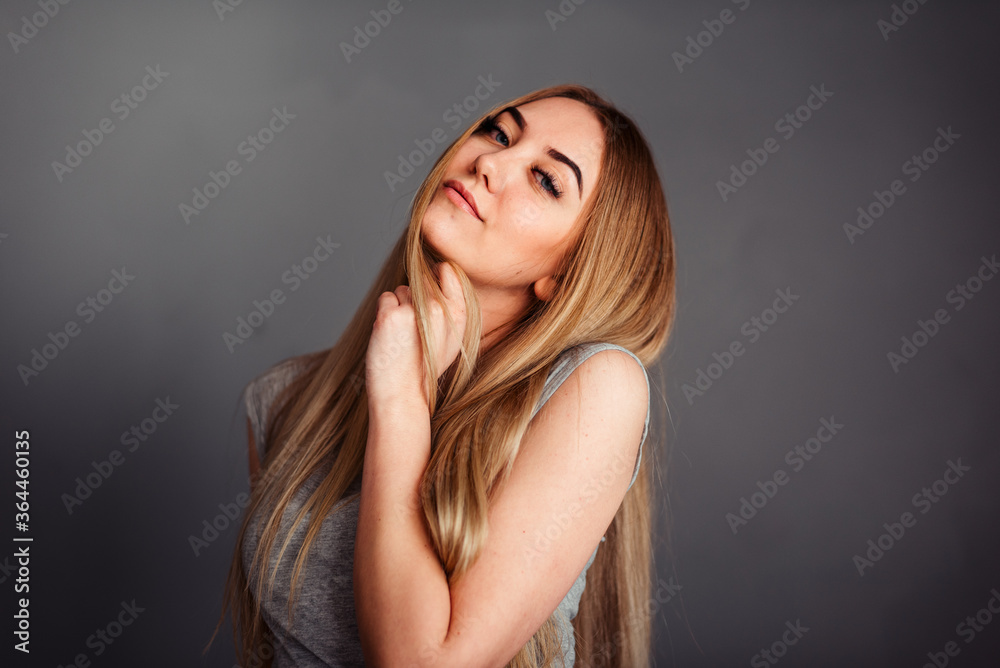 A girl with blue eyes looks piercingly into the frame, wrapping her hair in a gray background A girl with blue eyes looks piercingly into the frame, wrapping her hair in a gray background
