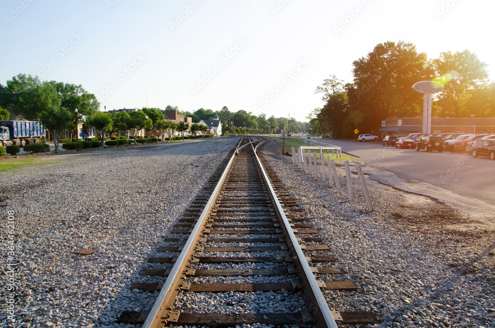 A low level view of a single track freight railway line leading straight into the distance, on the the edge of a small South Carolina town. The sun has just risen giving an orange glow