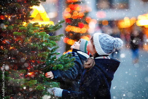 Two little kids, boy and girl having fun on traditional Christmas market during strong snowfall. Happy children enjoying traditional family market in Germany. Twins standing by illuminated xmas tree. photo