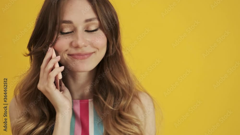 A close-up view of a pleased smiling young woman is talking on the phone isolated over a yellow background A close-up view of a pleased smiling young woman is talking on the phone isolated over a yellow background
