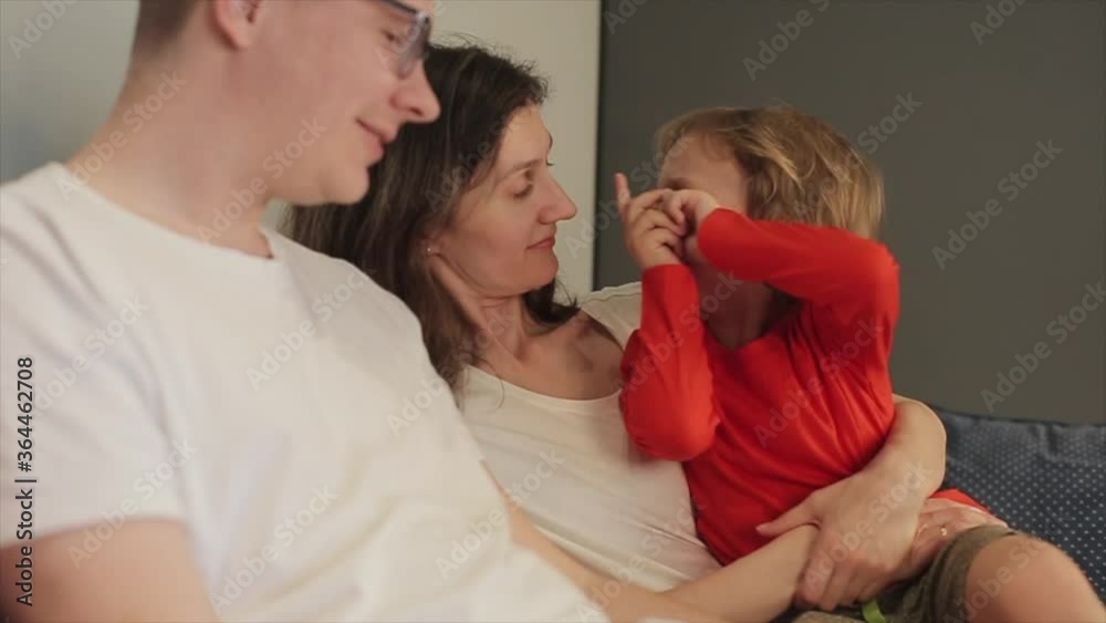 Young parents talk to their young son sitting on the couch and he is surprised and points the finger at his mother. Close-up Young parents talk to their young son sitting on the couch and he is surprised and points the finger at his mother. Close-up