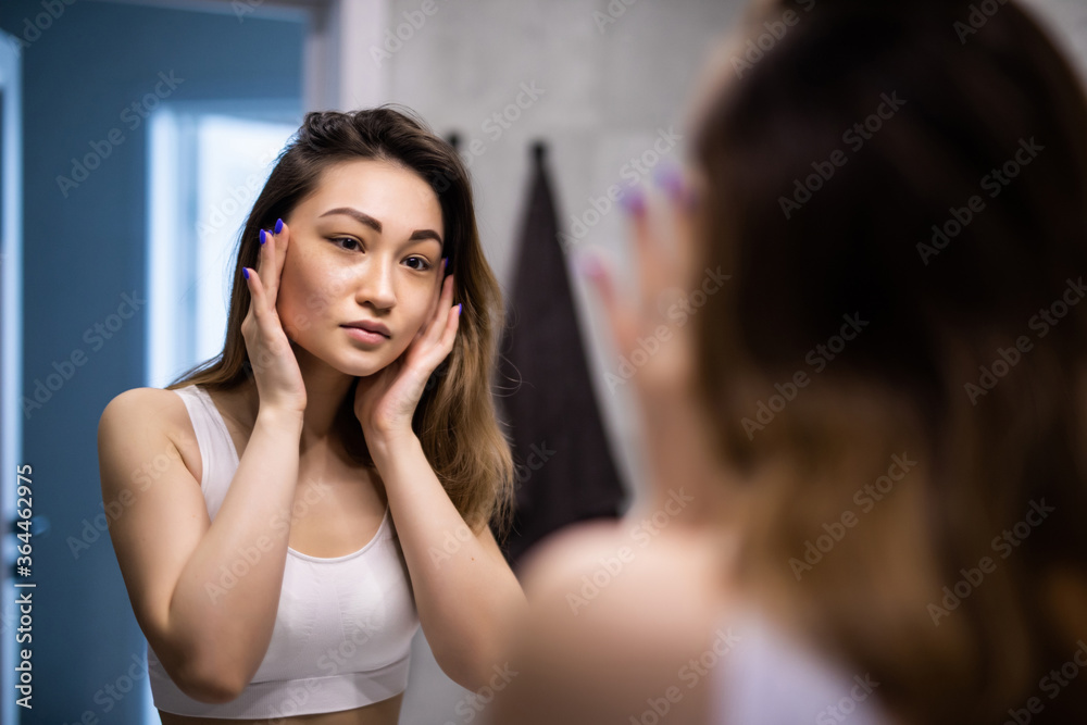 Young attractive asian woman caring her skin standing front of mirror in the bathroom Young attractive asian woman caring her skin standing front of mirror in the bathroom