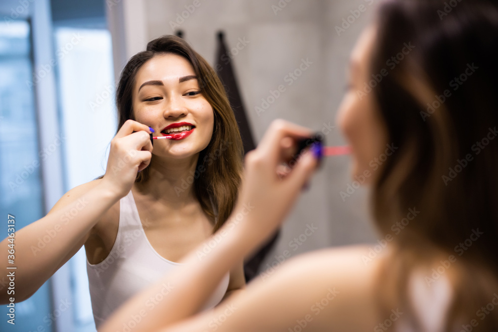 Young asian woman Lip gloss applied to her lips makeup in front of a bathroom mirror. . Young asian woman Lip gloss applied to her lips makeup in front of a bathroom mirror. .