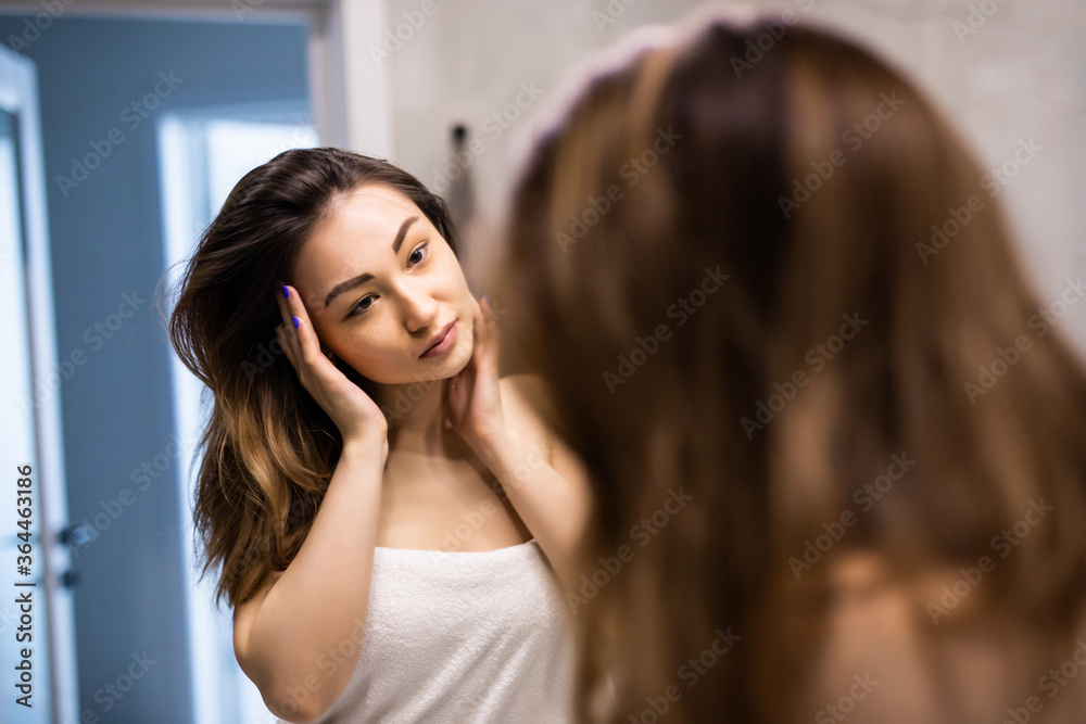 Young asian woman touching her face and looking to mirror in bathroom Young asian woman touching her face and looking to mirror in bathroom