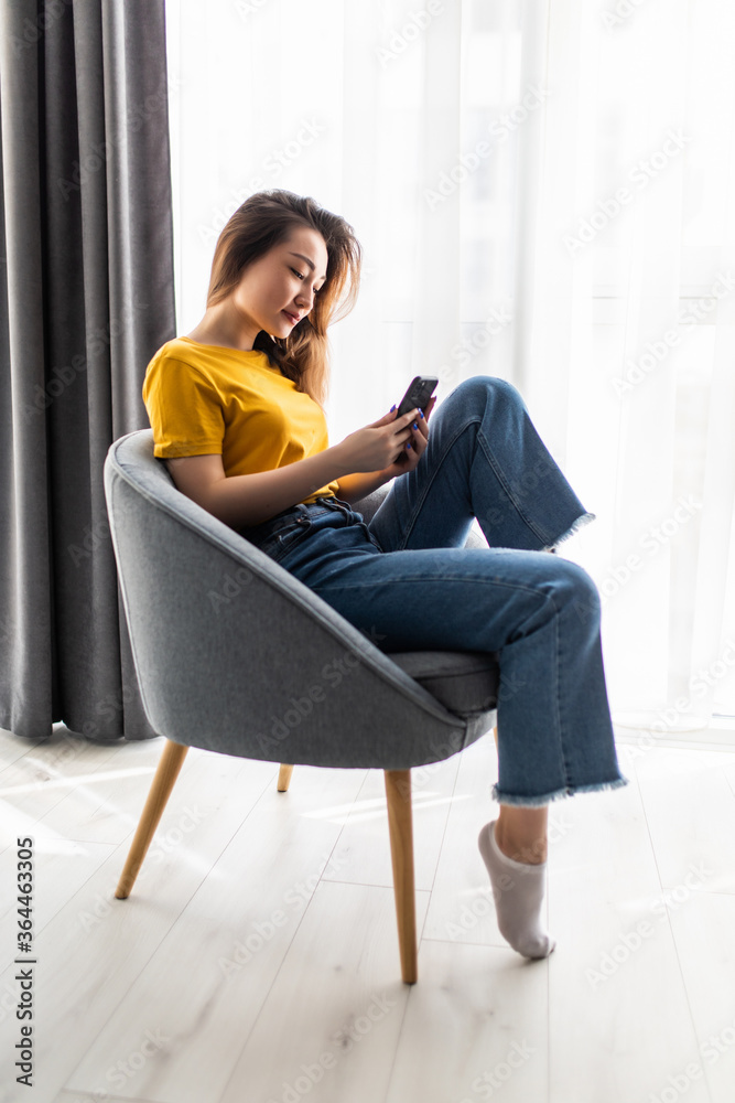 Portrait young asian woman using mobile phone sit on chair in living room interior Portrait young asian woman using mobile phone sit on chair in living room interior