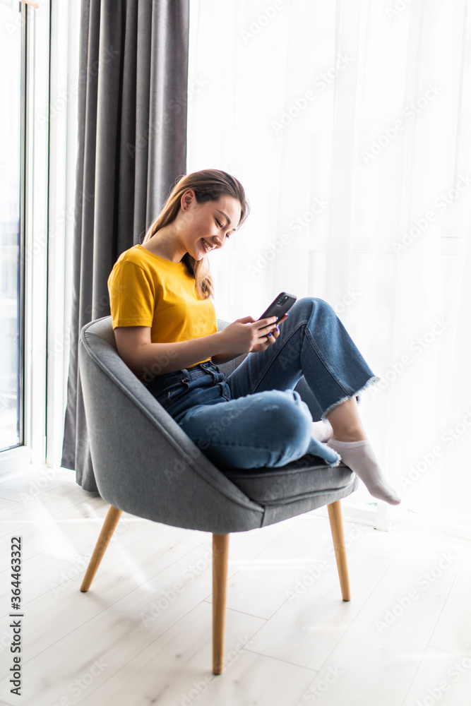 Young beautiful Asian woman relaxing in living room at home using phone in the morning with happy feeling Young beautiful Asian woman relaxing in living room at home using phone in the morning with happy feeling