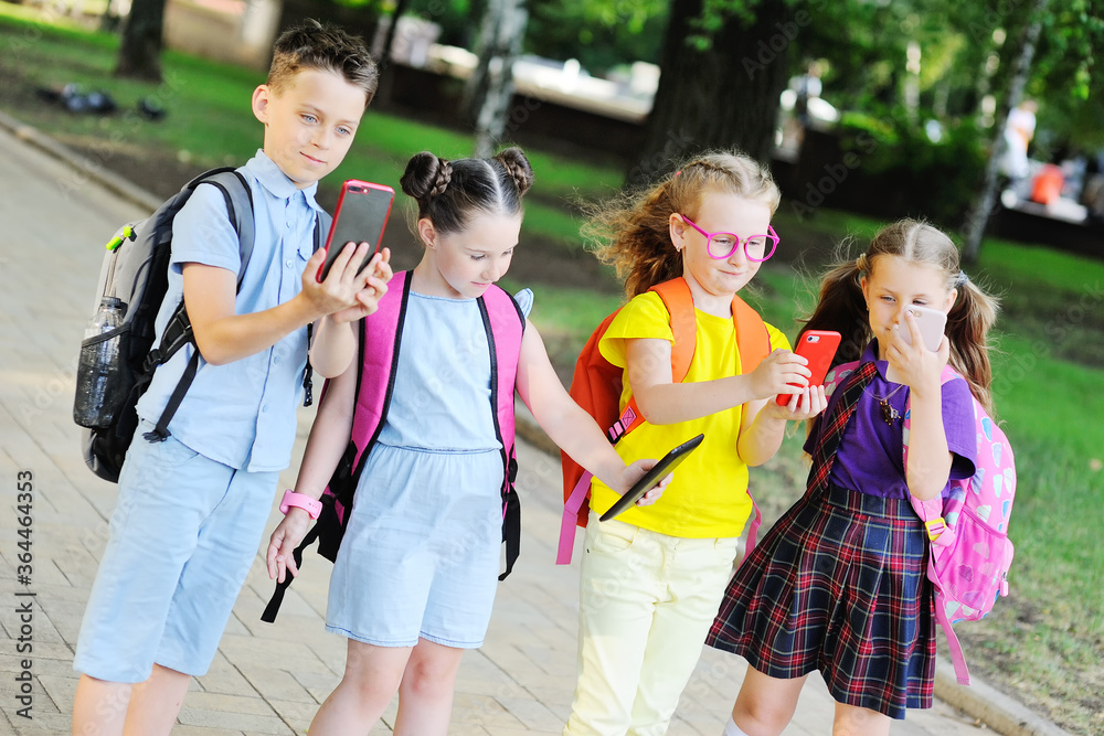 a group of school children in colorful clothes with school bags with smartphones in their hands go to school. Back-to-school gadgets, the day of knowledge, dependence on the mobile phone.