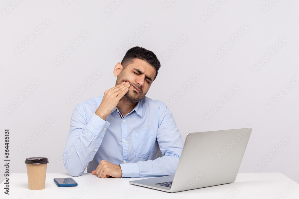 Sudden dental problems at work. Unhealthy man employee sitting in office, touching painful cheek, suffering acute toothache, inflamed gums, cavities or tooth decay. indoor studio shot isolated Sudden dental problems at work. Unhealthy man employee sitting in office, touching painful cheek, suffering acute toothache, inflamed gums, cavities or tooth decay. indoor studio shot isolated