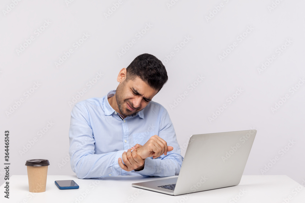 Male employee sitting office workplace with laptop, massaging sore wrist, suffering pinched nerve, stiff muscles, carpal tunnel syndrome after typing on computer. indoor studio shot, white background Male employee sitting office workplace with laptop, massaging sore wrist, suffering pinched nerve, stiff muscles, carpal tunnel syndrome after typing on computer. indoor studio shot, white background