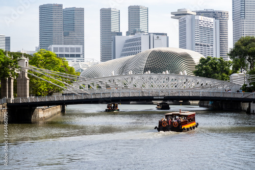 Photography Cavenagh Bridge, only suspension bridge and one of the oldest bridges in Singapore, with tourist boats and Singapore's skyline in the background