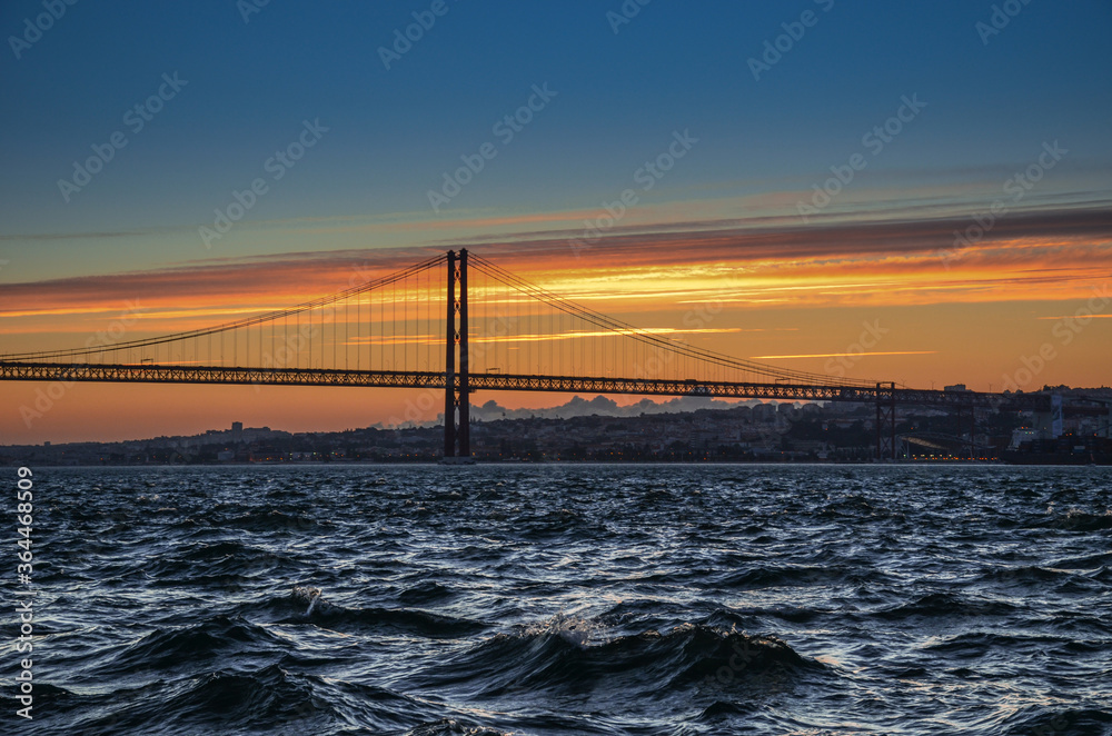 The 25th of April suspension bridge over the Tagus river, at sunset, in Lisbon, Portugal.