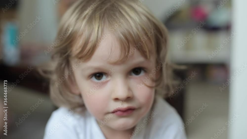 Portrait of a charming smiling blond little boy with curly hair and with big brown eyes in a white T-shirt. Close-up Portrait of a charming smiling blond little boy with curly hair and with big brown eyes in a white T-shirt. Close-up