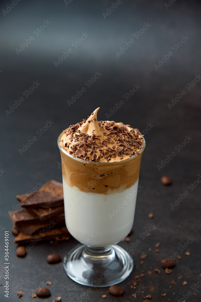 Glass of trendy fluffy creamy dalgona or whipped instant coffee with milk, coffee beans and chocolate on the dark background. New popular food and drink trend concept. Copy space. Glass of trendy fluffy creamy dalgona or whipped instant coffee with milk, coffee beans and chocolate on the dark background. New popular food and drink trend concept. Copy space.