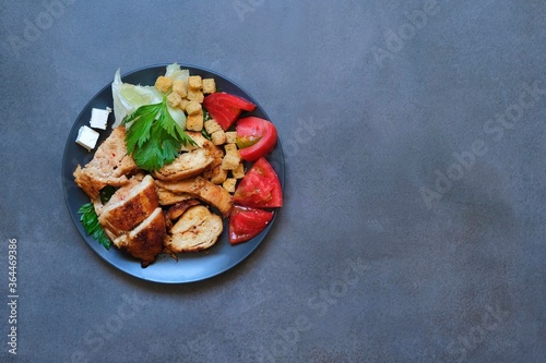 Pieces of baked chicken with tomato, cheese, crackers and herbs on a dark gray background. Top view.