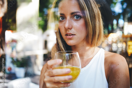 View though the window of a attractive female drinking a glass of fresh orange juice, young happy caucasian woman enjoying natural and vitamin beverage in home, gorgeous girl refresh with useful drink