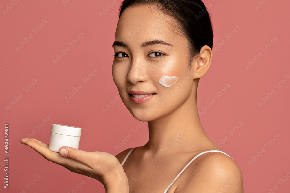 Asian beauty model concept. Moisturizing. Attractive young woman posing with face cream Asian beauty model concept. Moisturizing. Attractive young woman posing with face cream