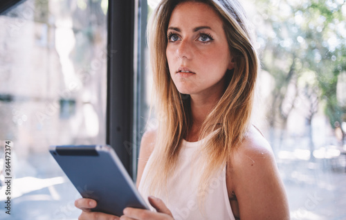 Free Download Portrait of a young charming businesswoman holding touch pad while standing near window in office interior, attractive female using her portable digital tablet for remote job during recreation time - GFXLoad