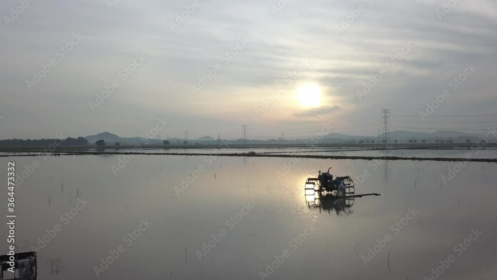 Move toward two tractors is flooded field with sun at background. Move toward two tractors is flooded field with sun at background.