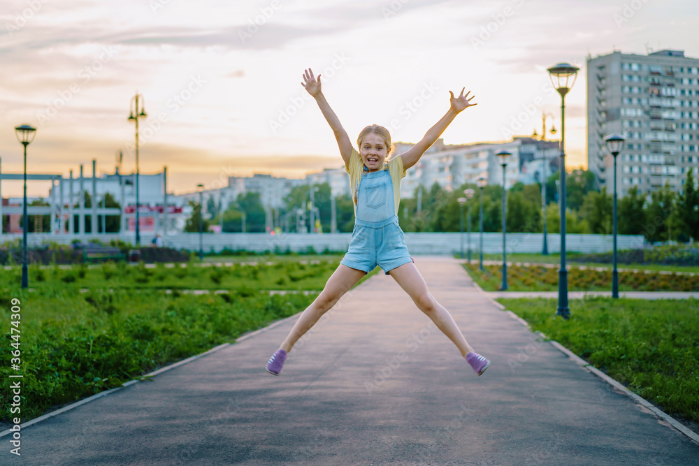 Happiness, activity and the concept of a child-a smiling little girl in a denim jumpsuit jumps on the street Happiness, activity and the concept of a child-a smiling little girl in a denim jumpsuit jumps on the street