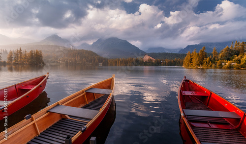 Beautiful sunny landscape. View on mountain lake with crystal clear azure water in High Tatras. Slovakia. Red Boats on the water glowing in sunlight at sunset. Awesome Autumn landscape. Strbsce pleso