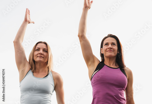 Two women working out doing stretch exercises outdoors raising their arms in the air in a low angle view in a healthy active lifestyle concept