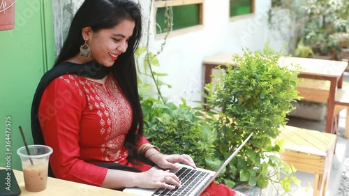 Young Indian woman in a cafe working on her laptop on her own blog and smiling