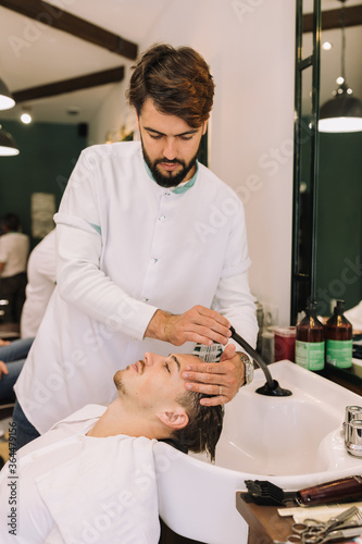 handsome barber washing a young brown man's hair at the barbershop wash 