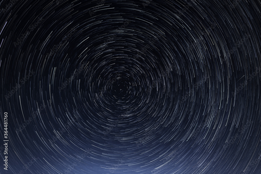 Stellar trails, the rotation of bright stars at night around the Polar Star against a blue sky and a meteor. The galactic vortex. Stellar trails, the rotation of bright stars at night around the Polar Star against a blue sky and a meteor. The galactic vortex.