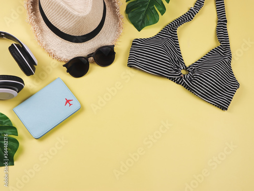 Travel and summer holiday concept, top view of black and white stripe pattern bikini swimsuit , passport and women's vacation accessories items on yellow background