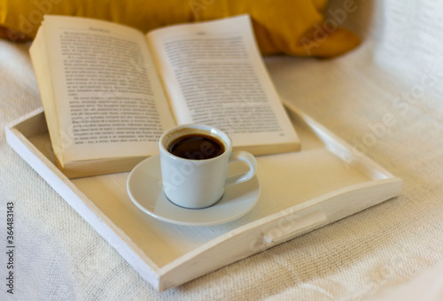 A small Cup of coffee and an open book against a warm blanket.The concept of relaxing in a cozy home environment.