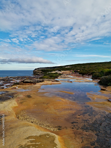 Beautiful coastal trail with colorful rock formations and reflections of blue sky on water puddles near Wattamolla Beach  Royal National Park  New South Wales  Australia