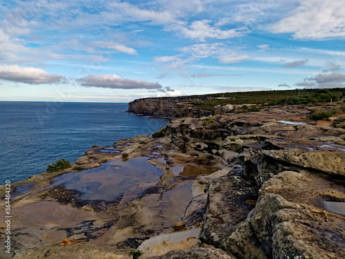 Beautiful coastal trail with colorful rock formations and reflections of blue sky on water puddles near Wattamolla Beach, Royal National Park, New South Wales, Australia 