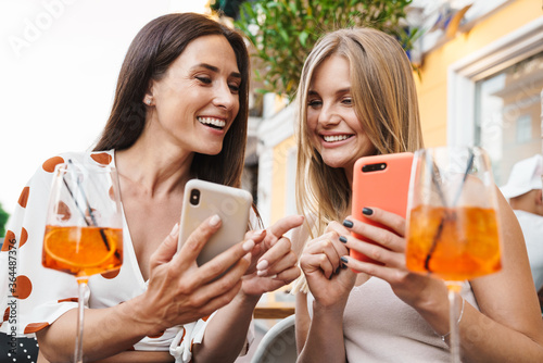 Image of women smiling and using cellphones while drinking cocktails