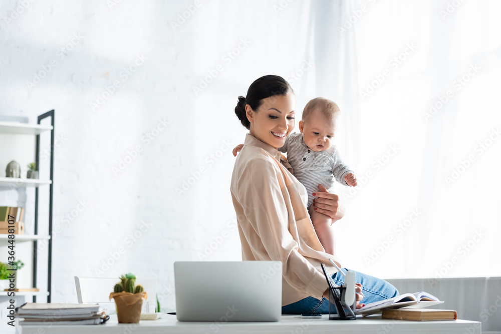 happy mother looking at notebook and holding in arms infant son