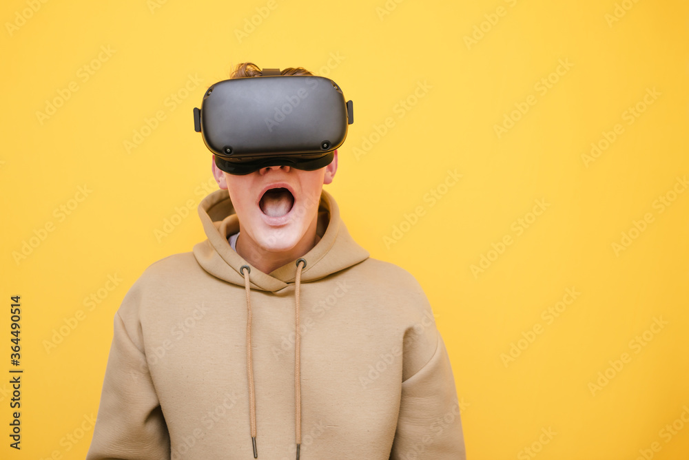 Closeup portrait of shocked guy in VR helmet on yellow background, looking into camera, copy space aside. Emotional teen gamer playing games in VR helmet. Closeup portrait of shocked guy in VR helmet on yellow background, looking into camera, copy space aside. Emotional teen gamer playing games in VR helmet.