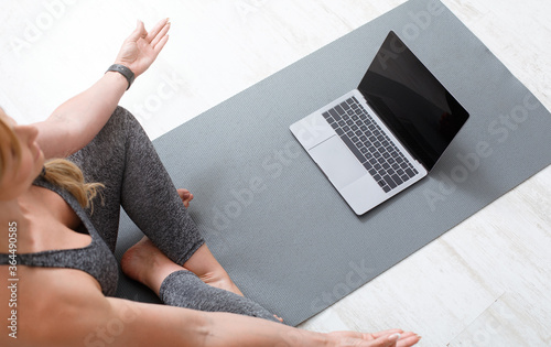Workout at home online. Woman meditating in lotus pose on floor on sport mat with laptop