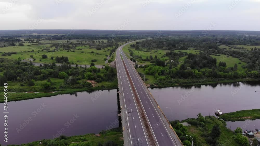Slow shooting from the copter of a wide road bridge over the river and a panorama of green meadows and forests overlooking the horizon