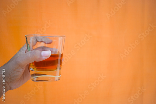 hand holding a glass of whiskey against orange background