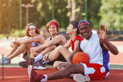 Happy African American basketballer and his multiracial team relaxing after match at outdoor stadium, free space © Prostock-studio