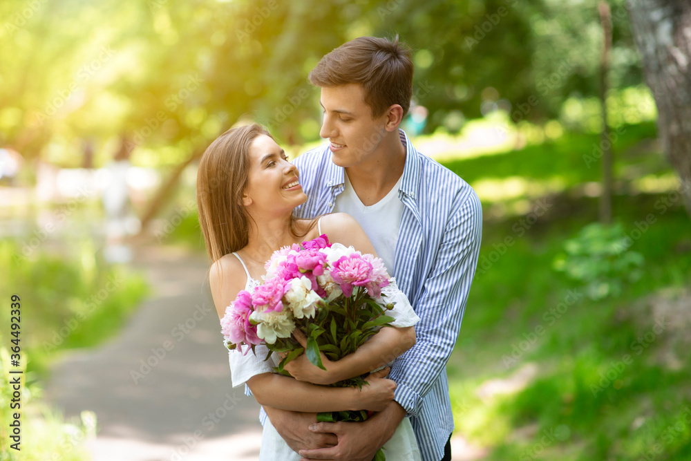 Young husband and wife with flower bouquet celebrating birthday outside on summer day Young husband and wife with flower bouquet celebrating birthday outside on summer day
