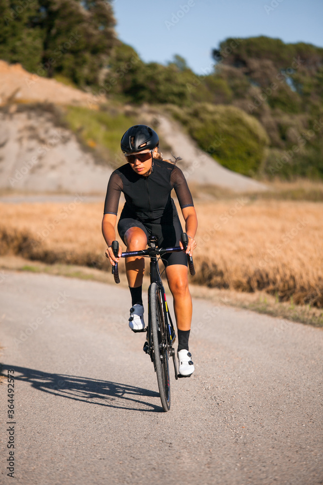 Obraz premium Pretty athlete woman dressed in black lowers her road bike quickly in a country setting.